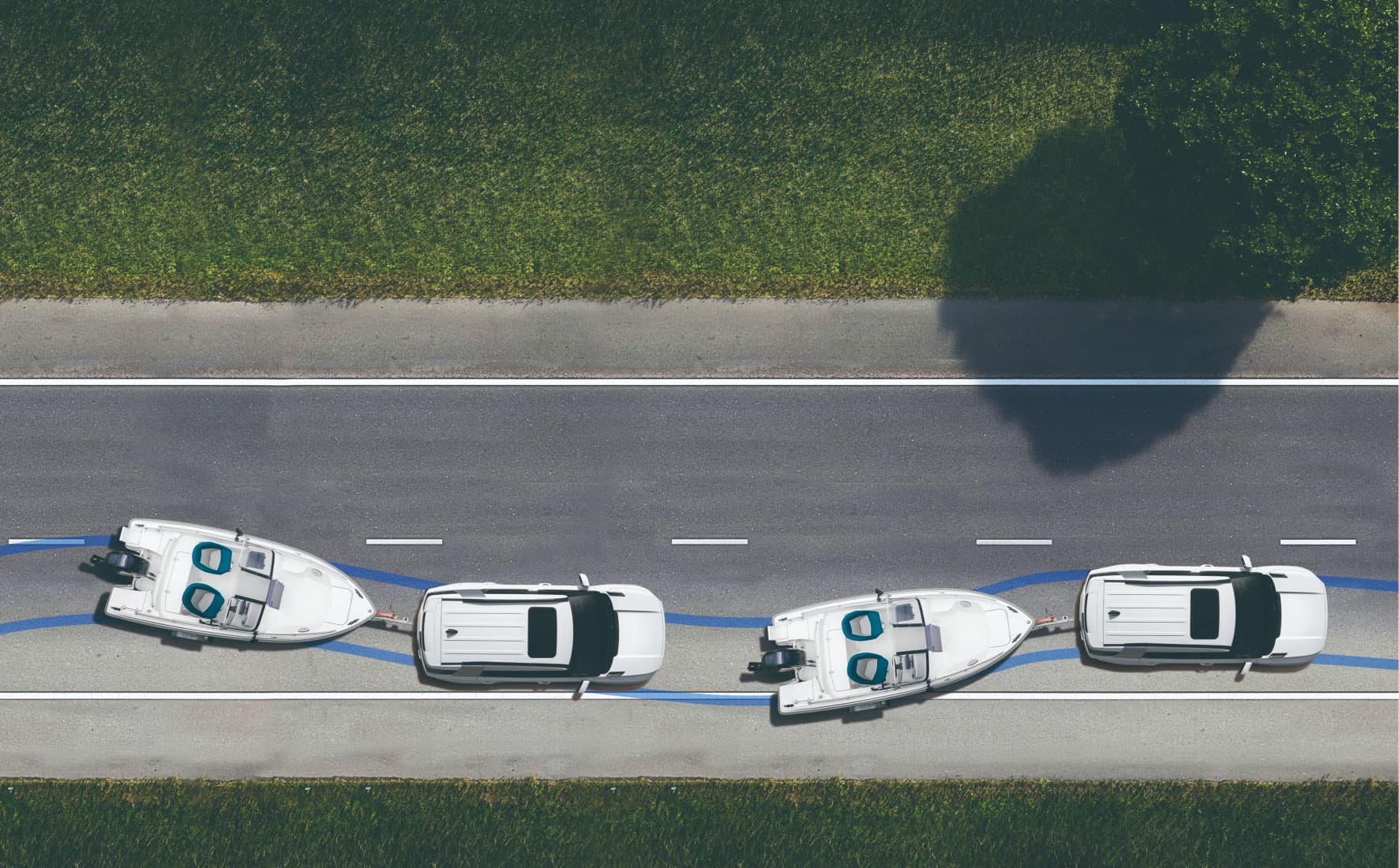 Aerial view of three white cars towing boats on a two-lane road, with a shadow of a tree on the right.