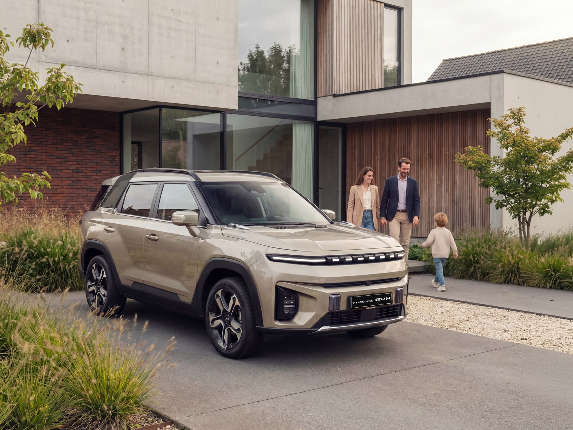 A modern Torres EVX is parked in front of a contemporary house. A family of three walks toward the entrance, with greenery surrounding the pathway.