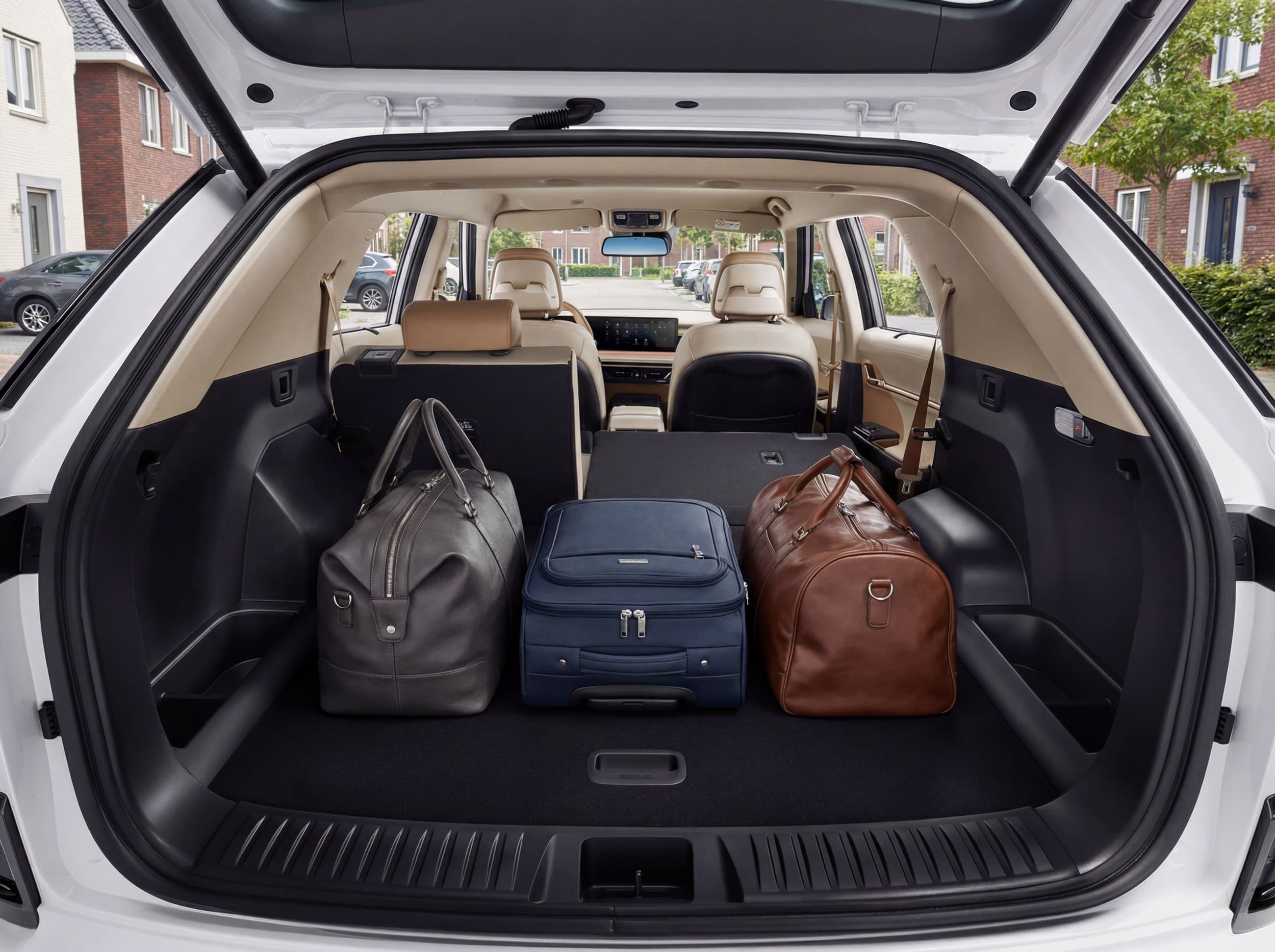 Open Actyon trunk with three bags inside: a gray duffel, a blue suitcase, and a brown duffel. The background shows residential houses.